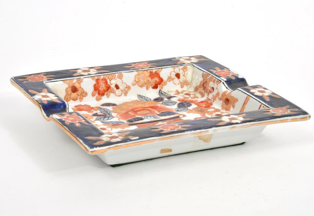 Imari-Style Porcelain Cigar Ashtray: Imari-style porcelain two-finger cigar ashtray, features center imagery of bouquet of flowers in vase, bordered by eating floral pattern with dark blue background, gilt edges. Green felt underside. Me
