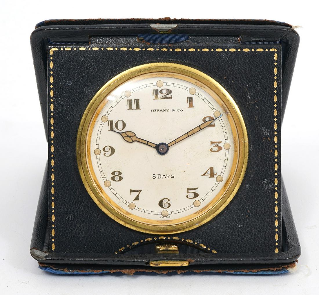 Tiffany & Co Folding Deco Travel Desk Clock: Tiffany & Co folding travel 8-day desk clock, deco style round face brass case. Leather and blue fabric frame. Measures 4"L x 4"W, and 3.5"H opened. Condition report: AS-IS condition, common wear to l