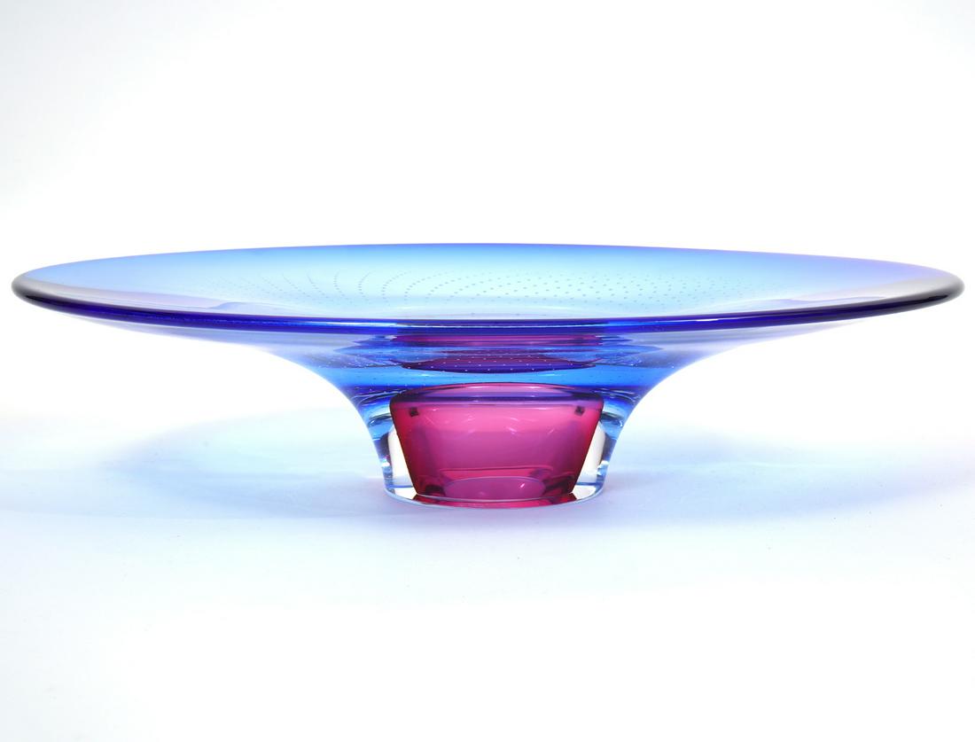 Kosta Boda Goran Warff Centerpiece Signed: Kosta Boda Swedish art glass footed centerpiece, signed by artist Goran Warff. Features blue and red hues with an array of small suspended bubbles. Measures 13"L x 9.5"W x 3"H. Condition report: Good