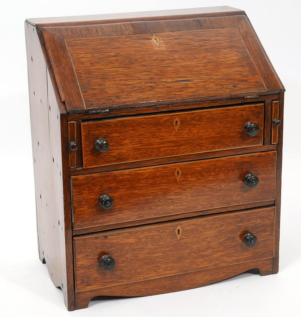 Miniature English Slant Front Secretary Desk: Miniature English secretary desk, features three front drawers and slant front hinged desk with additional drawers. Inlaid wood escutcheon, ebonized wood knobs. Back mounts for hanging on wall. Measur