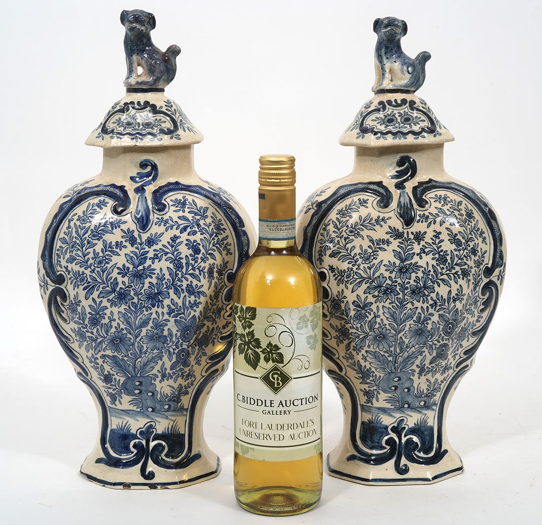 Pair of Delft Dutch Blue & White Urns: Pair of Delft Dutch blue & white garniture urns, features foliage motif and dog finals. Possibly 18th Century. Measures 16.25"H x 7.25"W. Condition report: Chips to inside edges of lid and underside e