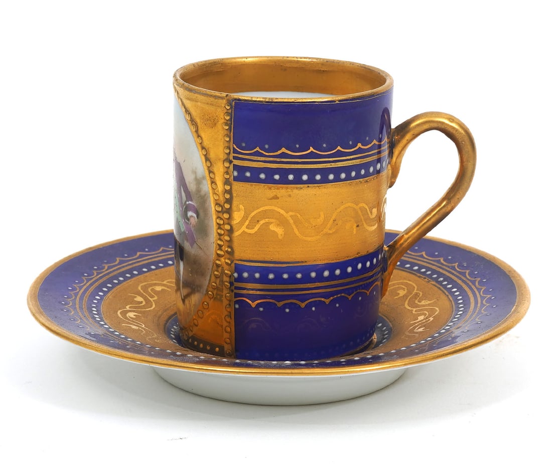 Royal Vienna Cobalt & Gilt Cup and Saucer: Royal Vienna cobalt and gilt cup and saucer with raised enamel decoration, features oval romantic scene. Blue beehive mark underside both. Measurements: saucer (4"W) and cup (2"H). Condition report: G