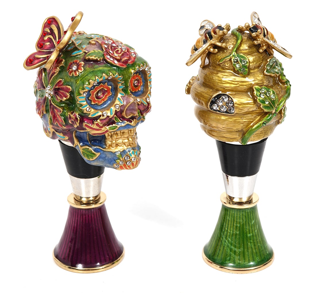 Jay Strongwater Enameled Jeweled Wine Stoppers: Jay Strongwater enameled jeweled wine bottle stoppers includes "Dia De Los Muertos" style skull with butterfly and a beehive stopper. Each rests on an enameled stand. Measures approx 4"H. Condition re