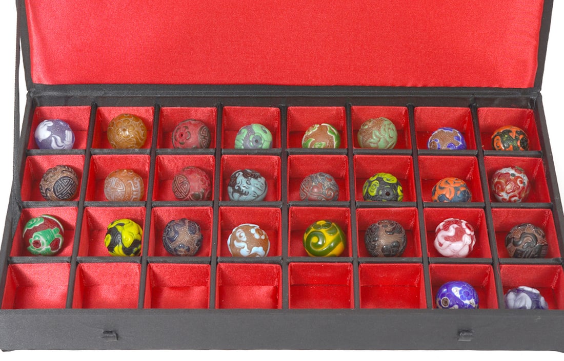 26 Chinese Glass Beads in Case: 26 Chinese multi-color carved glass beads in case, approximately 1" diameter. Case measures 12.5"L x 6.5"W x 2"H. Condition report: Good condition, please examine all photos closely. Contact C. Biddle