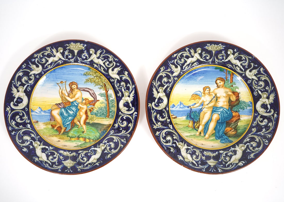 Pair of Italian Majolica Decorative Chargers: Pair of Italian Majolica decorative chargers with classical cherubic themes. Each measures 14" diameter. Condition report: Minor chips to edges, please see all photos. Contact C. Biddle Auction Galler