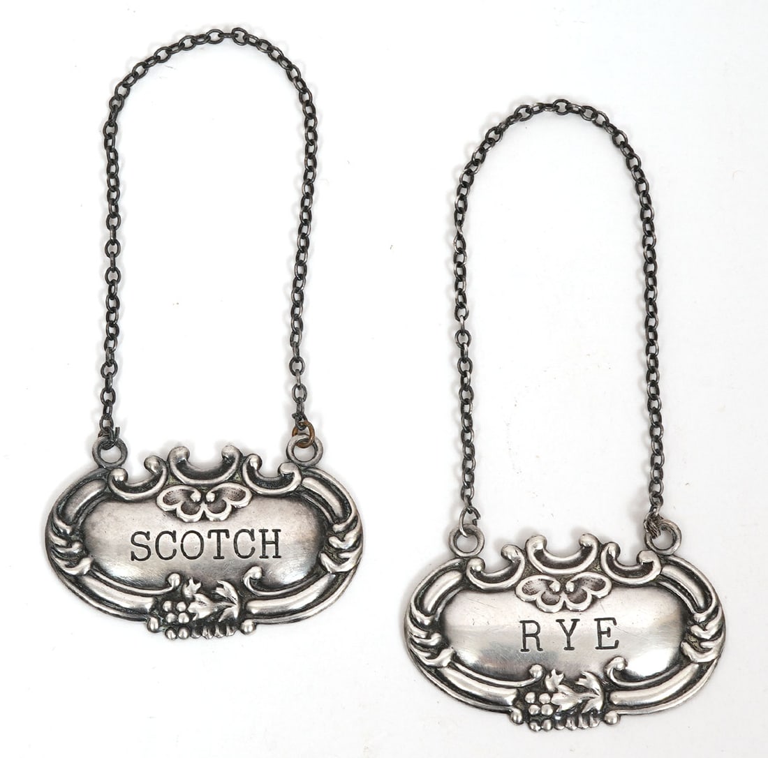 Sterling 'Scotch' and 'Rye' Liquor Tags: Sterling 'Scotch' liquor tag measures 1 1/8"H x 1 7/8"L and weighs 8.5 grams with a 6"L chain. 'Rye' tag measures the same and weighs 8.3 grams. Both tags have a 3" drop. Condition report: good condit