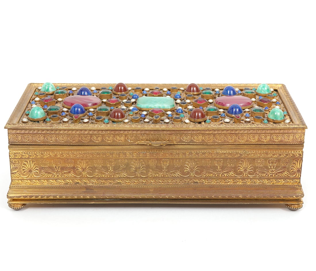 Gilt Bronze Jeweled Wood Lined Casket: Gilt bronze jeweled casket has intricate metal work, is inset with multicolored stones, small pearls and lined in wood. It is raised on 4 small circular feet and measures 7 3/8"L x 3 3/8"W x 2 3/8"H.