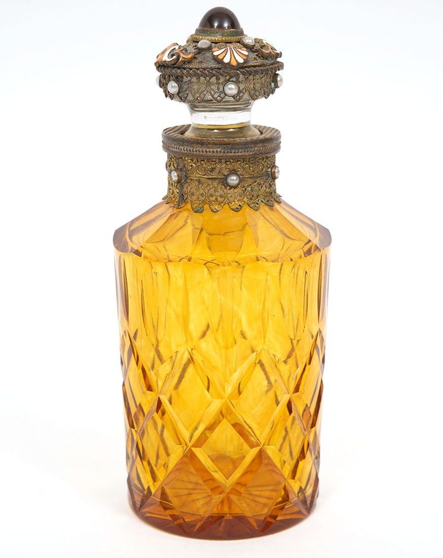 Antique Amber Perfume Bottle With Jeweled Stopper: Antique amber glass perfume bottle has a jeweled decorative stopper with matching trim around the neck. The glass body has sliced cut geometric patterns. Measures 5"H x 2"W. Condition report: good con