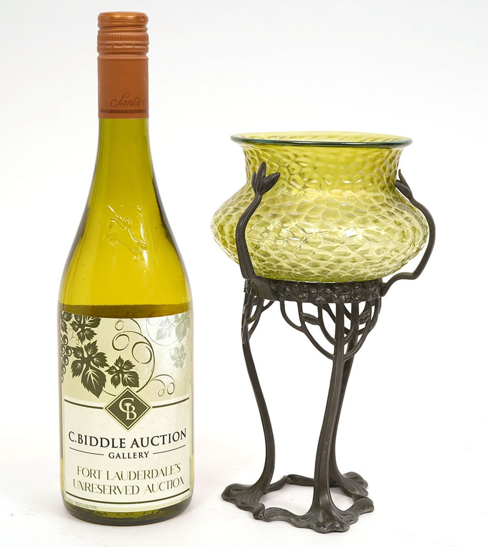 Art Nouveau Loetz Glass in Bronze Tripod Stand: Art Nouveau Loetz glass in bronze tripod stand features textured iridescent green glass vessel held by three armed bronze pedestal stand. Measures 9"H x 5.25"W. Condition report: Good condition, pleas