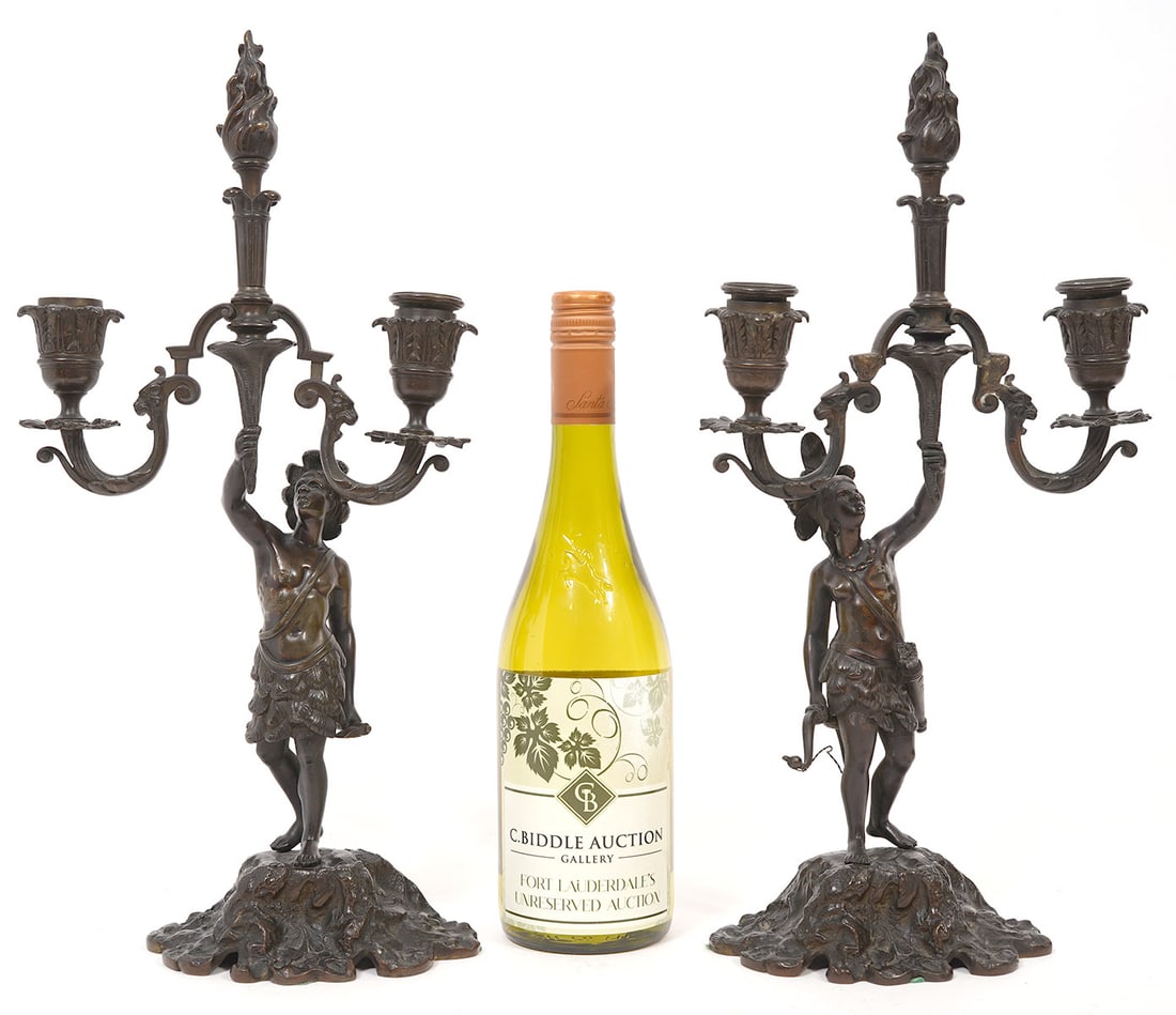 Pair of 19th C. Bronze Native Figural Candelabras: Pair of French 19th Century patinated bronze candelabras features male and female native figures holding up a torch. Measures 16"H x 8"W. Condition report: Some minor wear and bends for age and use, p