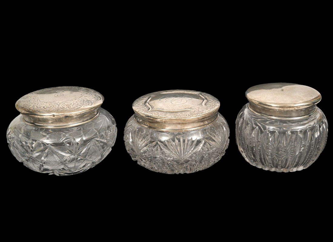 Three Sterling Top Cut-Crystal Vanity Boxes: Sterling top cut-crystal vanity boxes includes two boxes with engraved scrolling motif to sterling tops and cross-cut patterns to crystal (3"H x 4.5"W); Plain top with deep vertical cuts (3"H x 3.5"W)