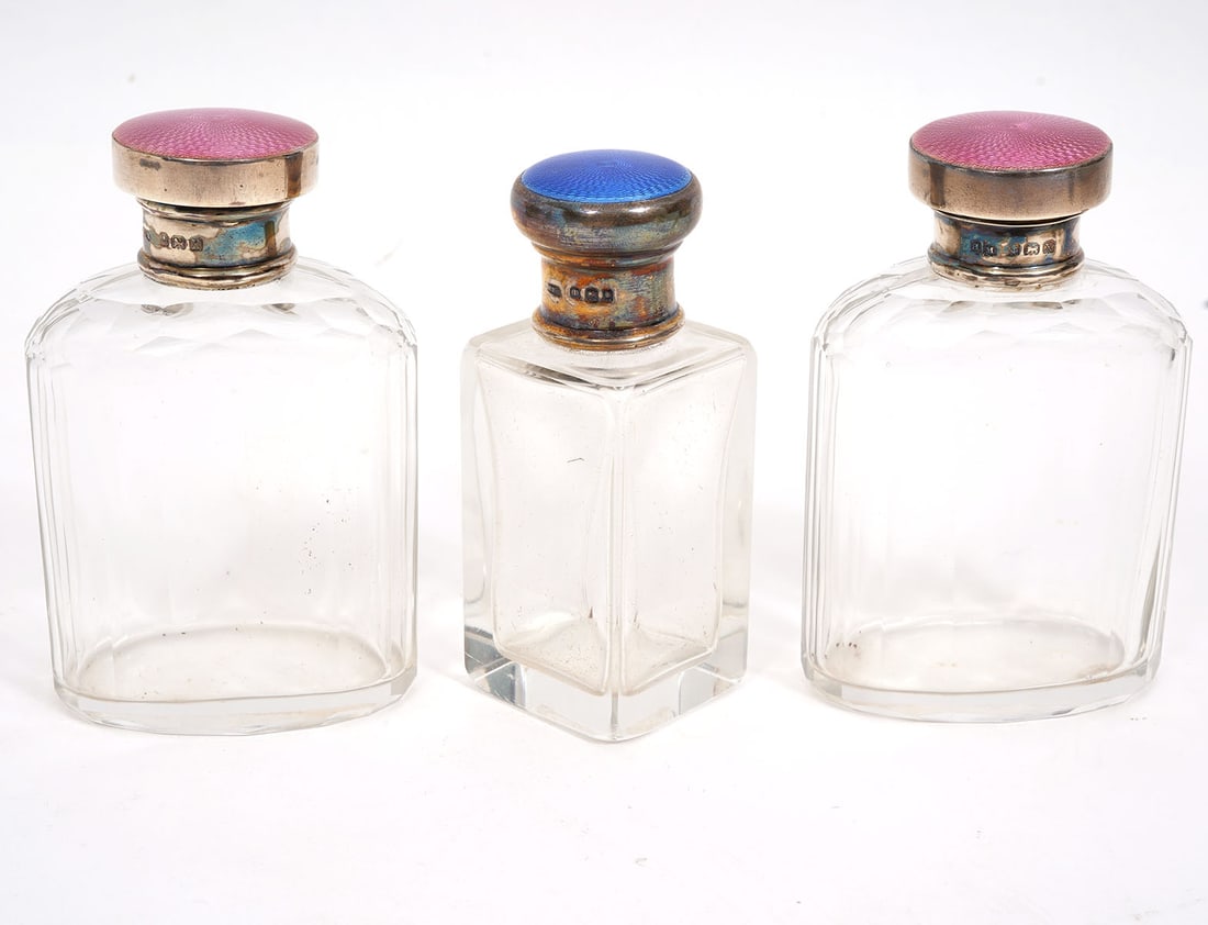 English Enamel on Silver Glass Vanity Bottles: English guilloche enamel on sterling silver glass vanity bottles. Lot includes: Two pink enamel bottles (3.75"H x 2.25"W), blue enamel square body bottle (3.5"H x 1.25"W). Condition report: Good condi
