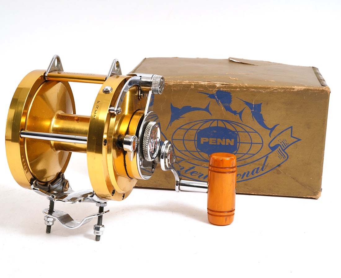Penn International 50 Fishing Reel: Penn International 50, gold-tone fishing reel. Original packaging. Measures 7.25"W. Condition report: Minor surface scratches, please examine all photos closely. Contact C. Biddle Auction Gallery for 