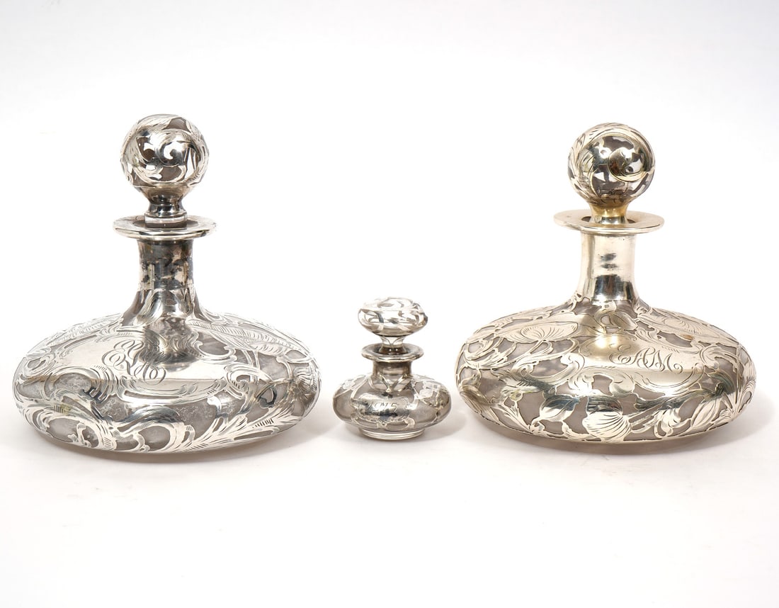 3 Sterling Silver Overlay Glass Perfume Bottles: Pair of sterling silver overlay glass perfume bottles, and an additional smaller bottle. Monogrammed. Features scrolling floral pattern with hand-engraved details on a wide body form bottle with spher