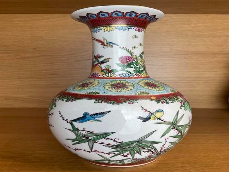 FAMILLE ROSE BOTTLE VASE: The bulbous body below a tall waisted neck, decorated with birds perched upon stalks of flowering peonies issuing from rocks, the shoulder decorated with stylized lotus scrolls on a ruby-red ground, a