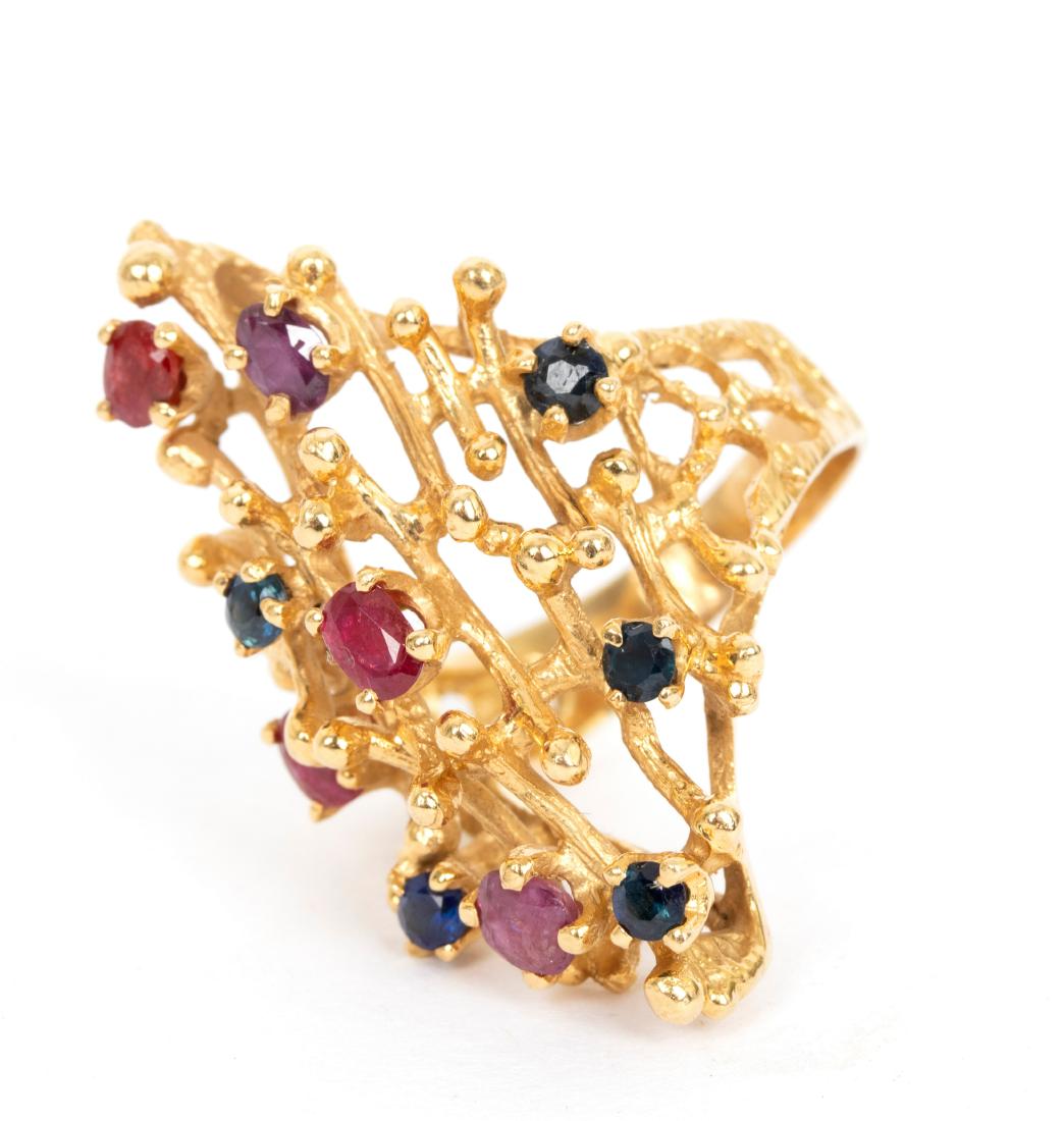A sapphire and ruby ring in the style of Andrew Grima,: A sapphire and ruby ring in the style of Andrew Grima, the textured openwork 18ct yellow gold setting set with scattered stones, size P, approximately 13.6gm/