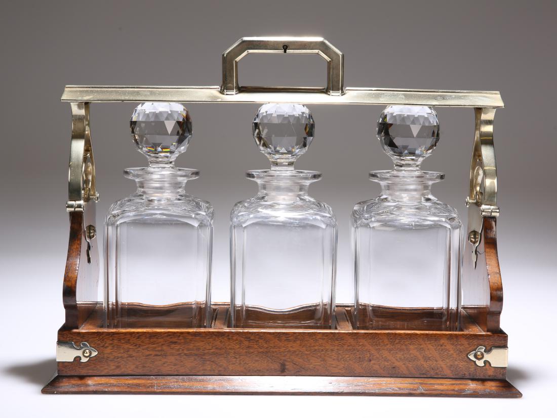 AN EDWARDIAN SILVER PLATE MOUNTED OAK PATENT TANTALUS,: AN EDWARDIAN SILVER PLATE MOUNTED OAK PATENT TANTALUS, with locking handle and three decanters, complete with key. 40.5cm long