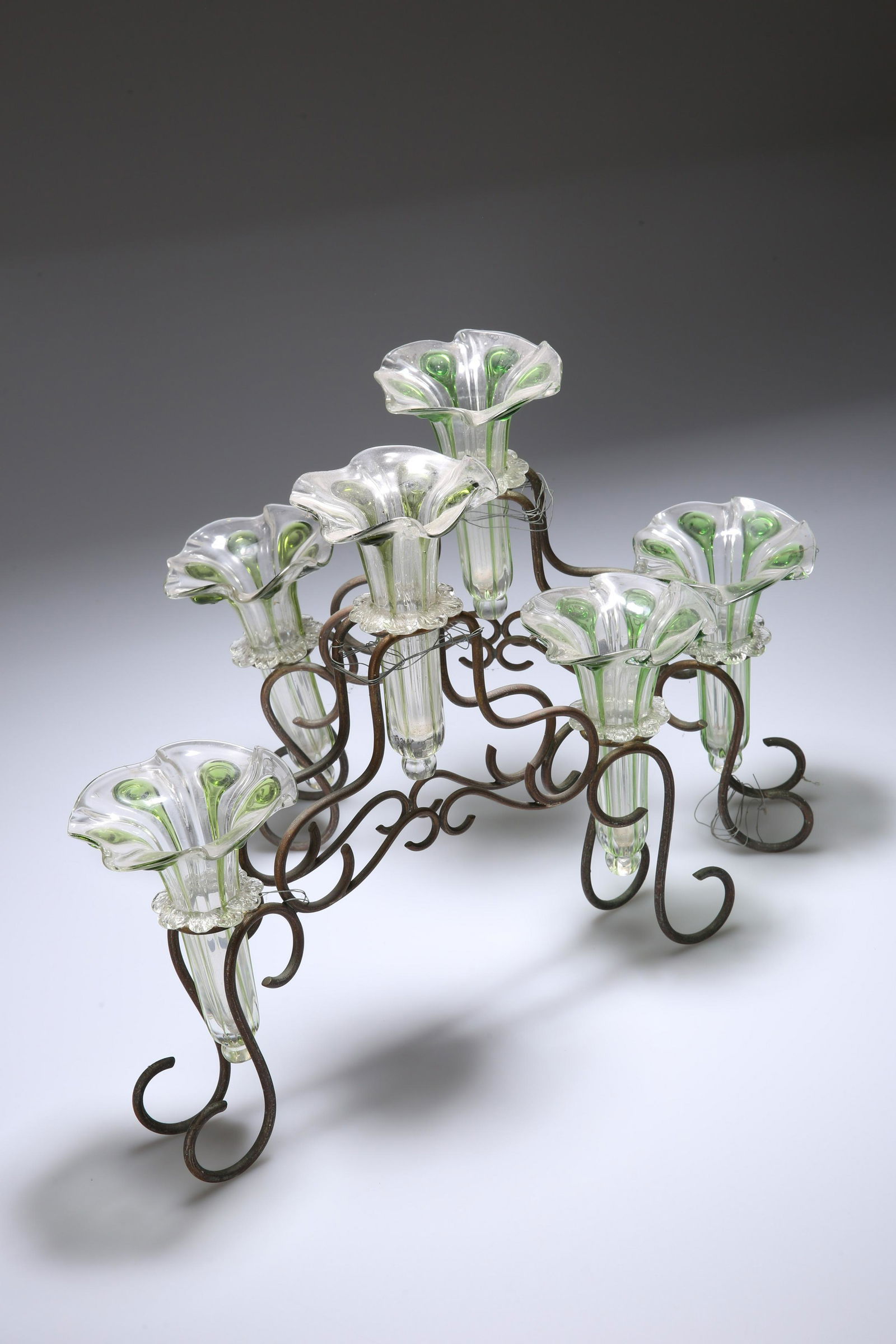 A PAIR OF ART NOUVEAU WROUGHT-IRON AND GLASS EPERGNES,: A PAIR OF ART NOUVEAU WROUGHT-IRON AND GLASS EPERGNES, each scrolling frame fitted with three moulded trumpets, possibly James Powell, each with green trailed decoration; together with three further t