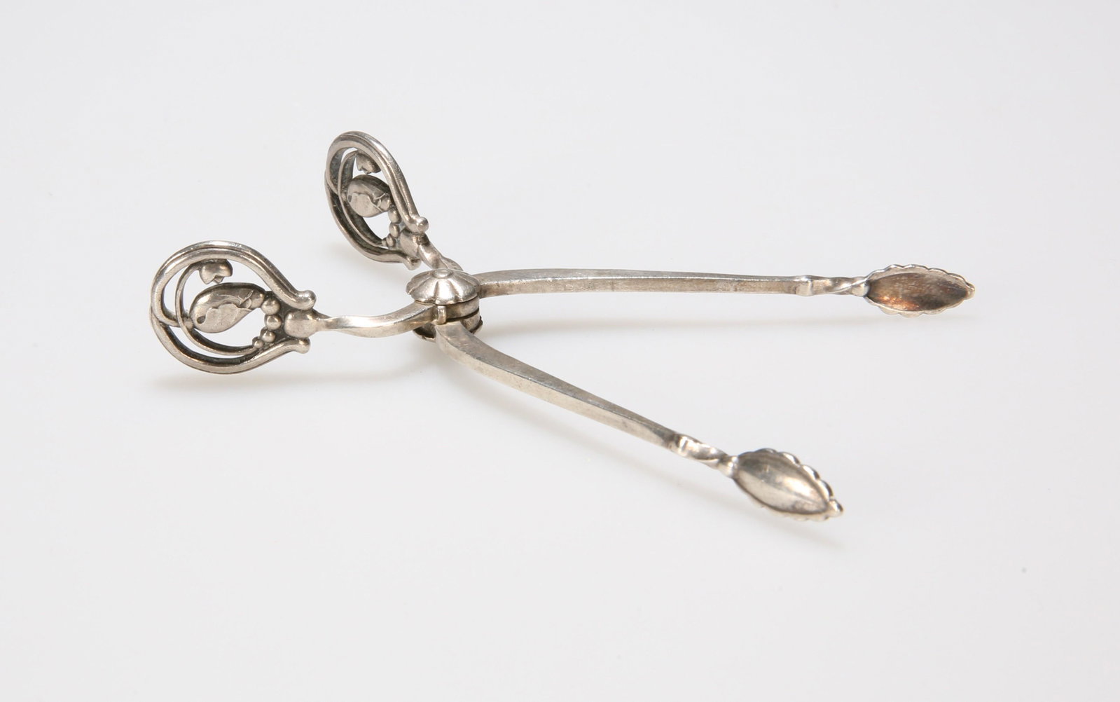 A PAIR OF DANISH SILVER SUGAR TONGS BY GEORG JENSEN,: A PAIR OF DANISH SILVER SUGAR TONGS BY GEORG JENSEN, IMPORT MARK FOR LONDON 1922, importer's mark for George Stockwell, with pierced blossom handles. 9cm