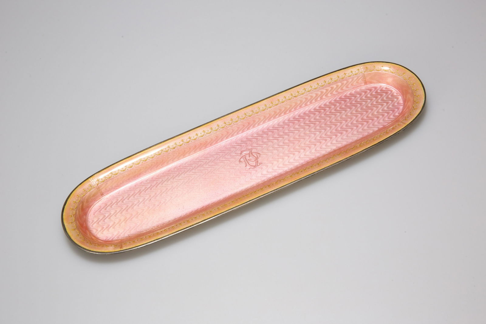 A DAVID ANDERSEN SILVER AND ENAMEL PEN TRAY, of rounded: A DAVID ANDERSEN SILVER AND ENAMEL PEN TRAY, of rounded rectangular form, the pink guilloche enamel ground centred by a monogram and bordered by conjoined gilt swags, signed and marked. 7.9 troy ounce