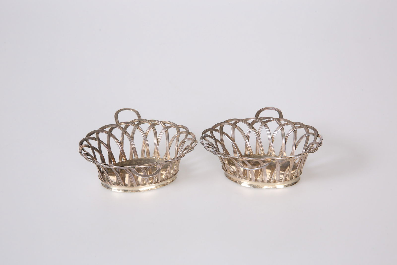A PAIR OF GEORGE III SILVER SWEETMEAT BASKETS, JOHN: A PAIR OF GEORGE III SILVER SWEETMEAT BASKETS, JOHN HENRY VERE & WILLIAM LUTWYCHE, LONDON 1765, oval with wirework structure and twin handles, each engraved with a crest. 4.7 troy ounces, 9.5cm by 11.