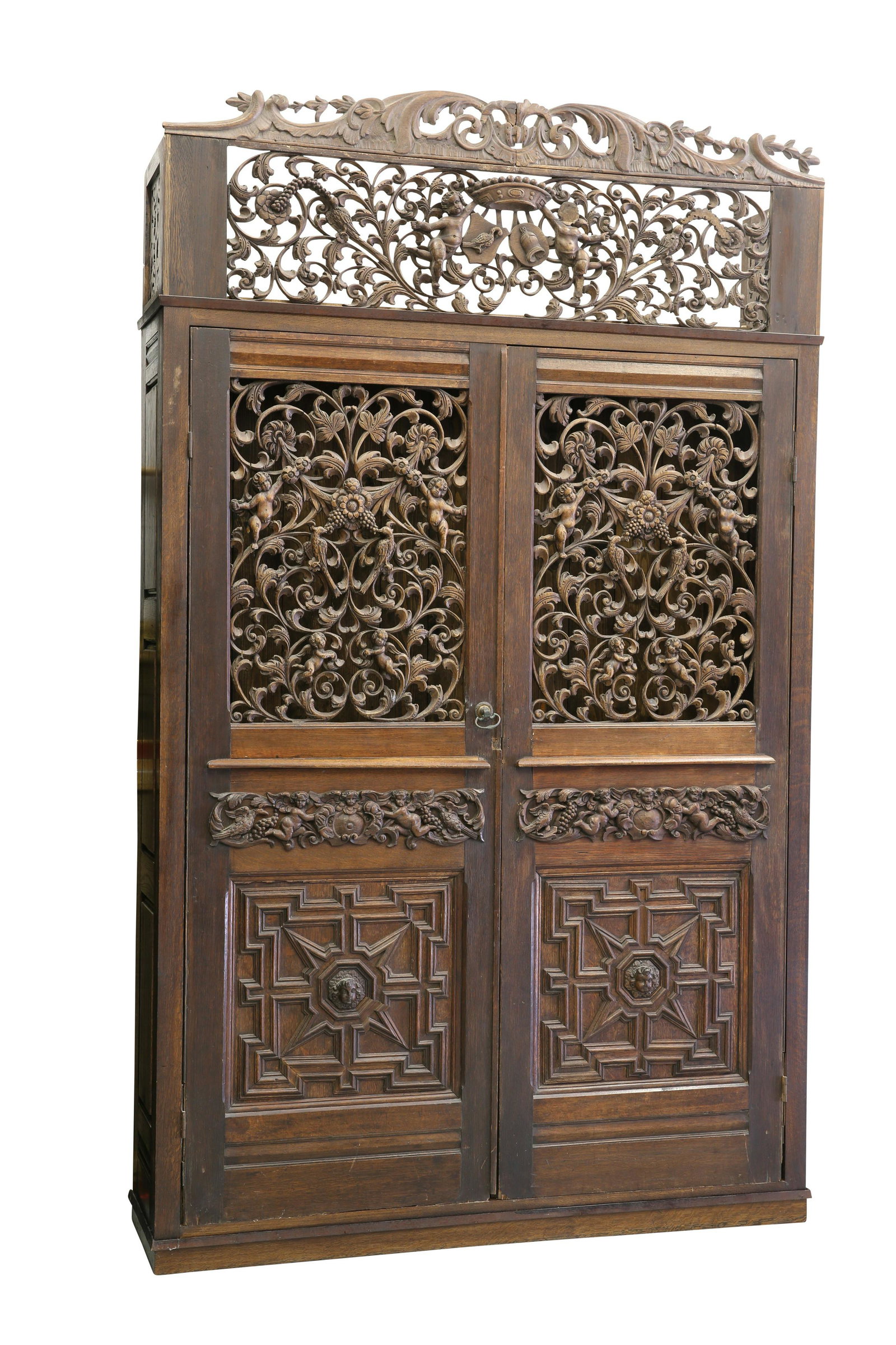 AN OAK CABINET, the cornice pierced and carved with: AN OAK CABINET, the cornice pierced and carved with crown, putti, birds and scrolls, above a pair of doors with carved and pierced panels. 241cm high, 146cm wide, 36cm deep Provenance: The Keith Sche