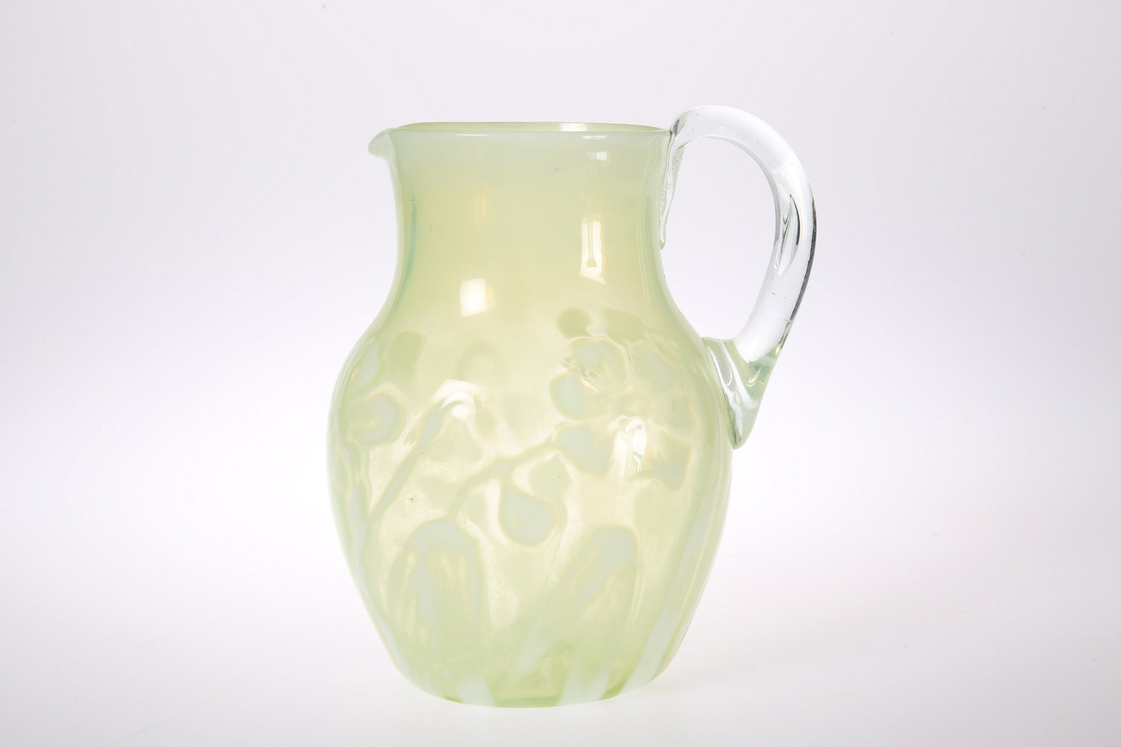 A LATE VICTORIAN VASELINE GLASS PITCHER Of baluster: A LATE VICTORIAN VASELINE GLASS PITCHER Of baluster form, moulded and picked out in opaline with stylised flowers, clear glass handle.Â 19cm.