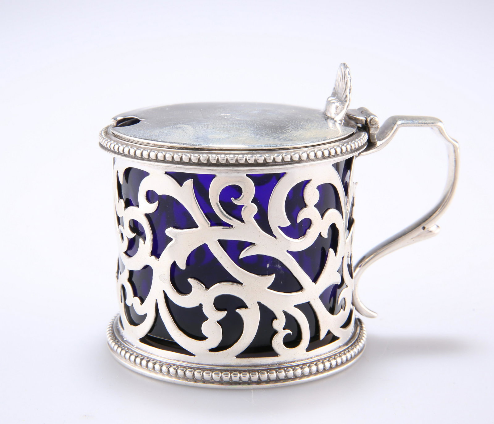 A VICTORIAN PIERCED SILVER MUSTARD POT, by Charles: A VICTORIAN PIERCED SILVER MUSTARD POT, by Charles Stuart Harris, London 1894, of cylindrical form, with hinged lid and scallop shell thumbpiece, S-scroll handle and foliate pierced body with bead dec