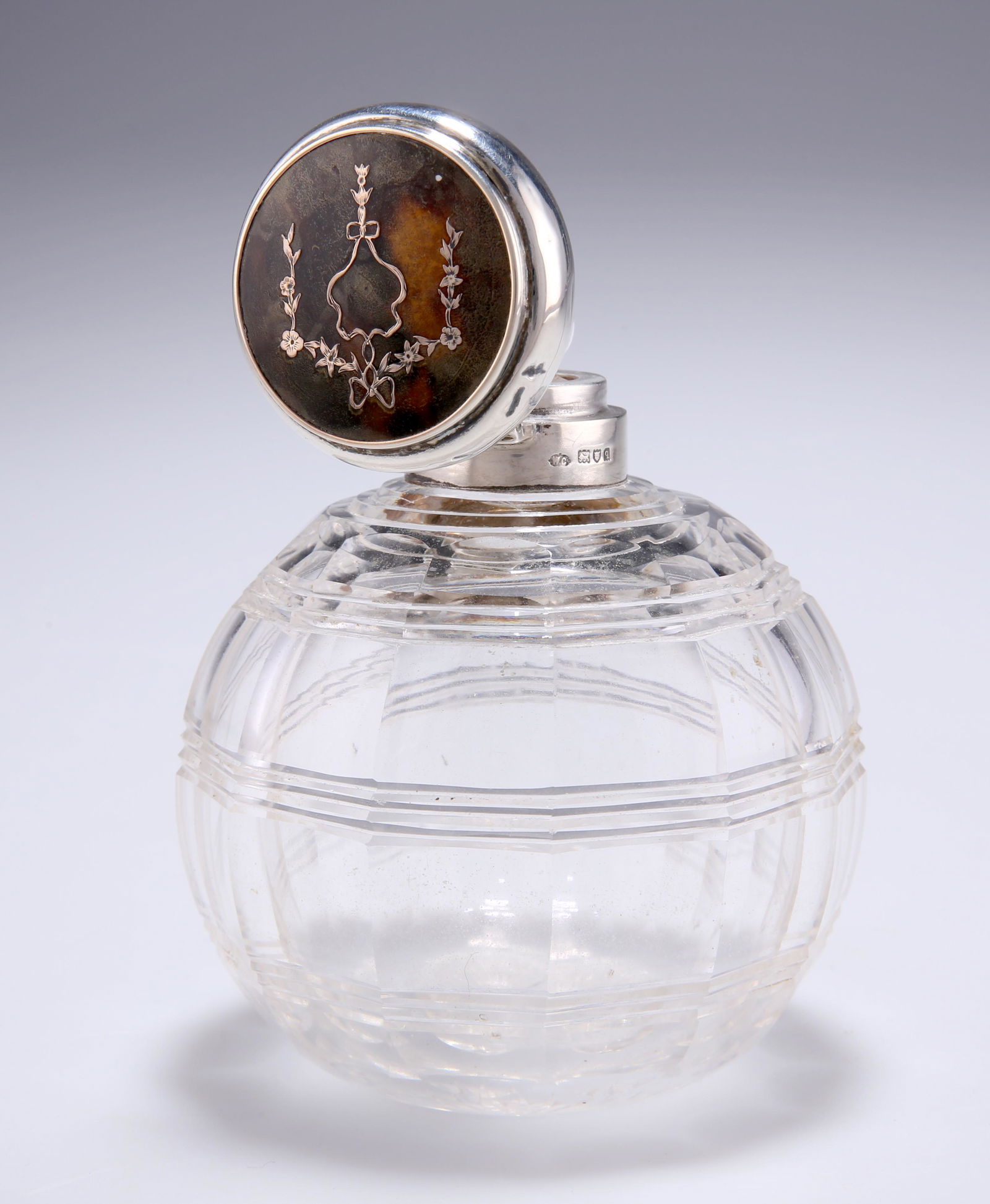 A GEORGE V SILVER AND TORTOISESHELL TOPPED CUT-GLASS: A GEORGE V SILVER AND TORTOISESHELL TOPPED CUT-GLASS SCENT BOTTLE, by William Comyns & Sons, London 1911, the hinged cover with pique decoration of floral garland, with original stopper. 10cm high