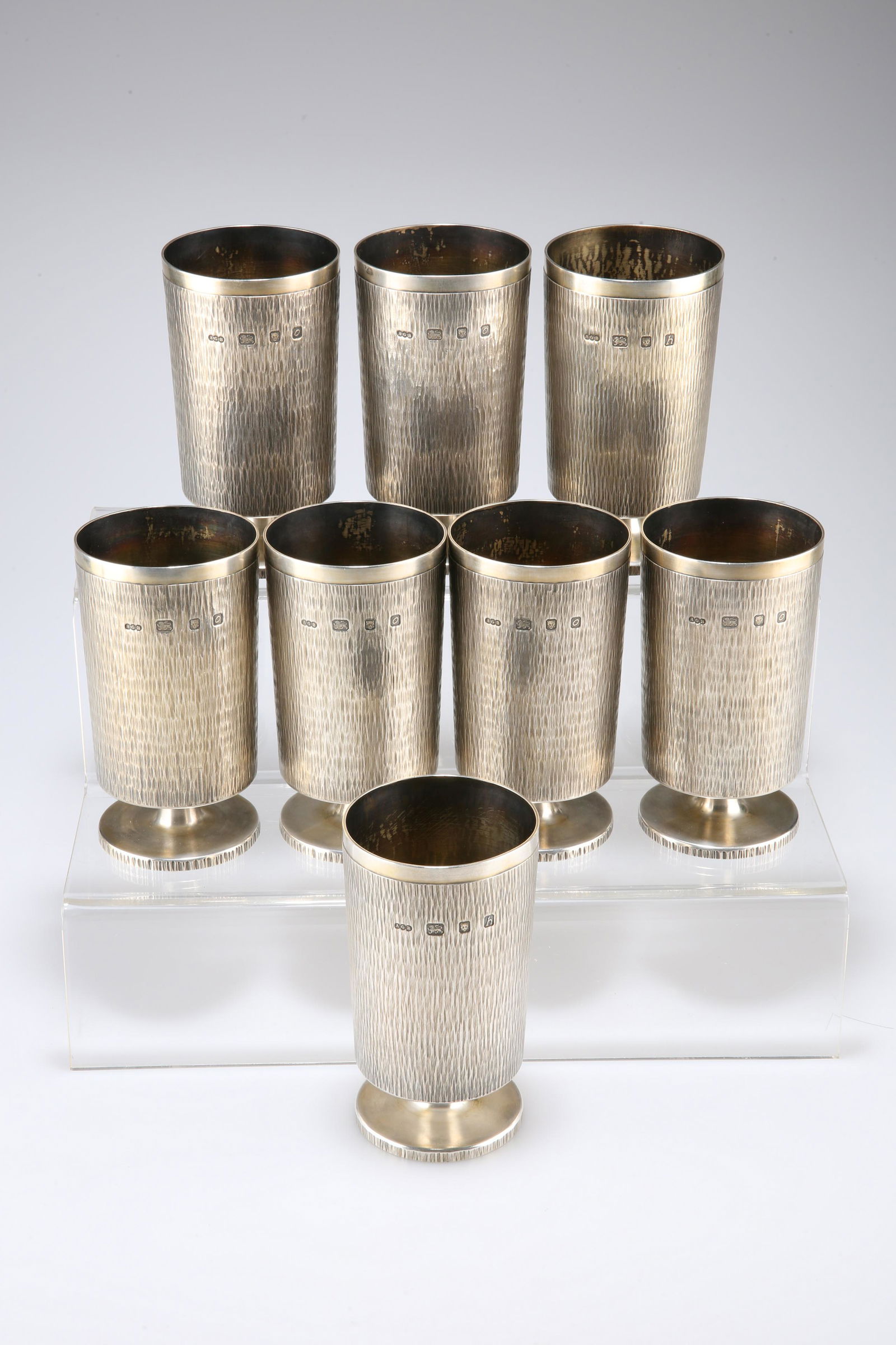 A SET OF EIGHT CONTEMPORARY GERALD BENNEY SILVER: A SET OF EIGHT CONTEMPORARY GERALD BENNEY SILVER GOBLETS, London 1963-69, each of cylindrical form with bark effect exterior raised upon pedestal circular foot rings, cartouche engraved RL-H. 12.8cm b