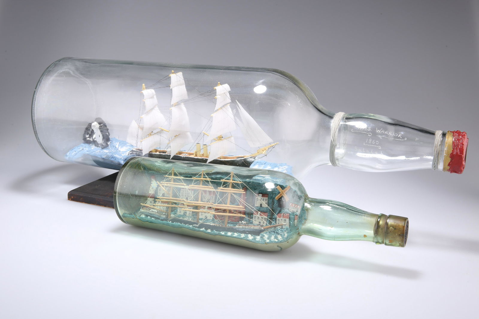 TWO MODEL SHIPS IN BOTTLES, HMS Warrior and 'Betty',: TWO MODEL SHIPS IN BOTTLES, HMS Warrior and 'Betty', the first on a wooden stand. First 50cm long overall