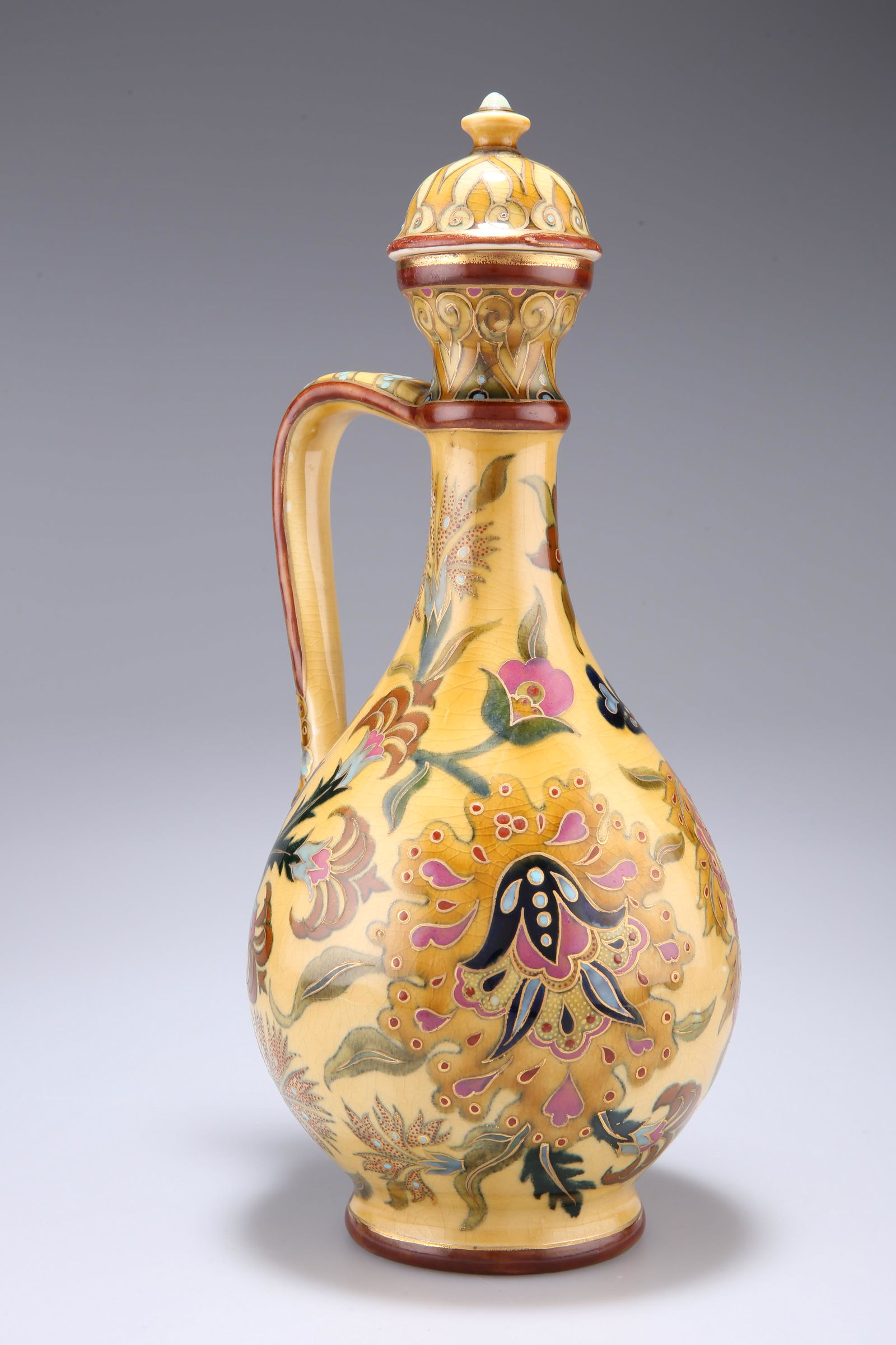 A ZSOLNAY PECS EWER AND COVER, CIRCA 1870-80, decorated: A ZSOLNAY PECS EWER AND COVER, CIRCA 1870-80, decorated in the Persian taste with foliage, the handle in the form of a snake, printed factory mark and painted number. 32cm high