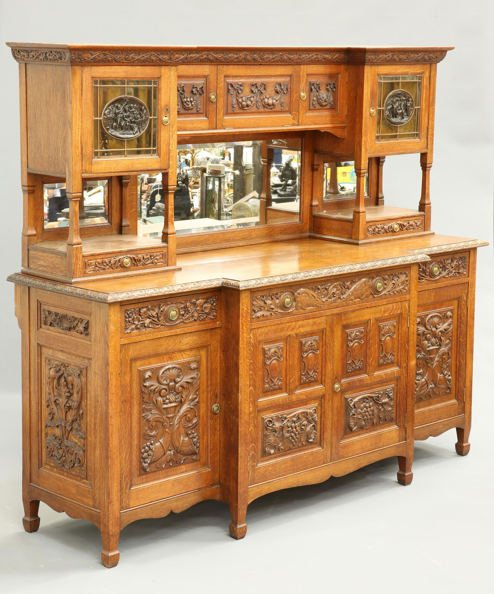 JOHN SHEARER FOR ARTHUR SIMPSON AN ARTS AND CRAFTS: JOHN SHEARER FOR ARTHUR SIMPSON AN ARTS AND CRAFTS OAK MIRROR BACK SIDEBOARD, the superstructure with a pair of fabric backed glazed doors each centred by patinated metal biblical panels signed Justin