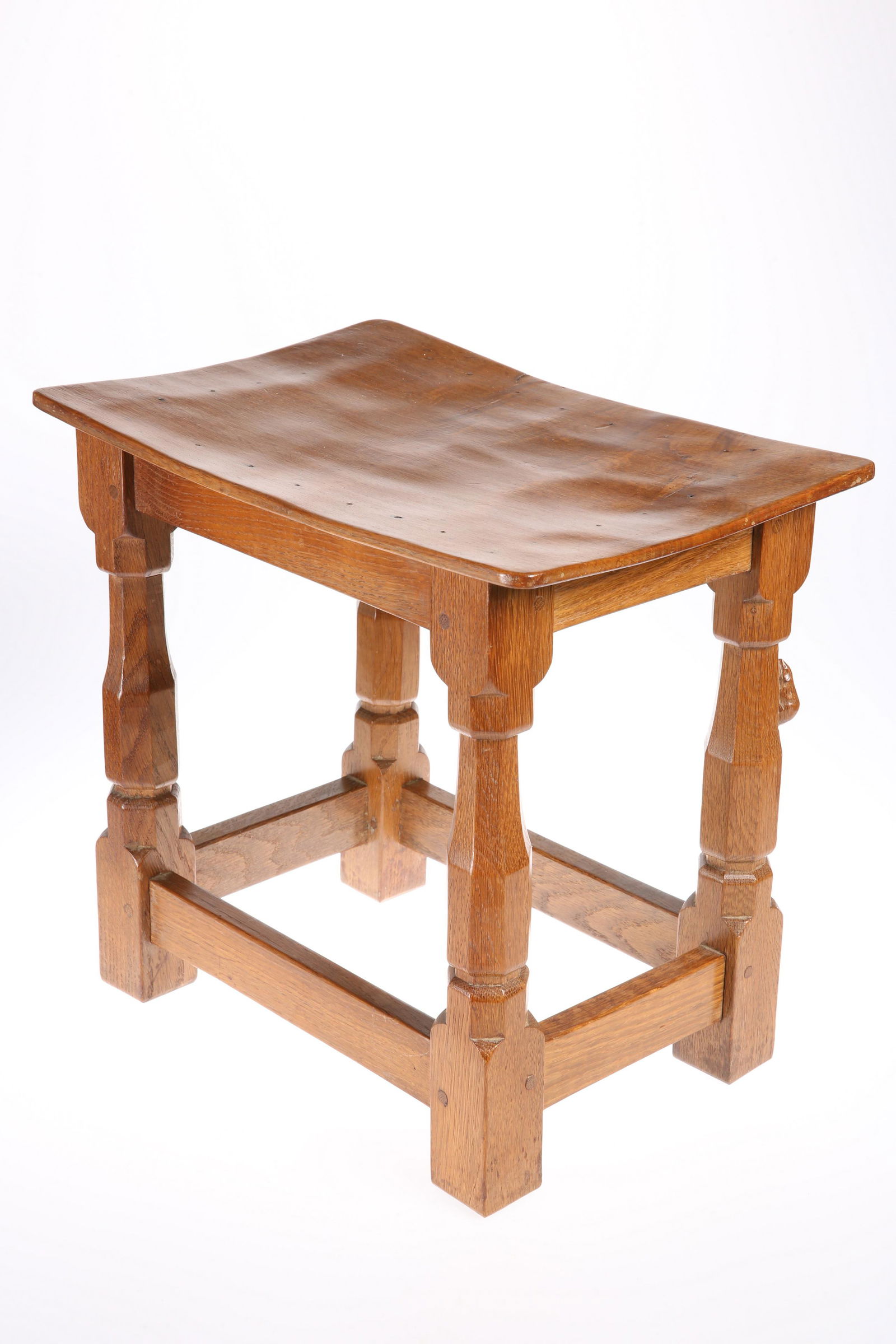 ROBERT THOMPSON OF KILBURN A MOUSEMAN OAK STOOL, the: ROBERT THOMPSON OF KILBURN A MOUSEMAN OAK STOOL, the dished rectangular top raised on faceted baluster legs terminating in blocks joined by stretchers. 37cm high