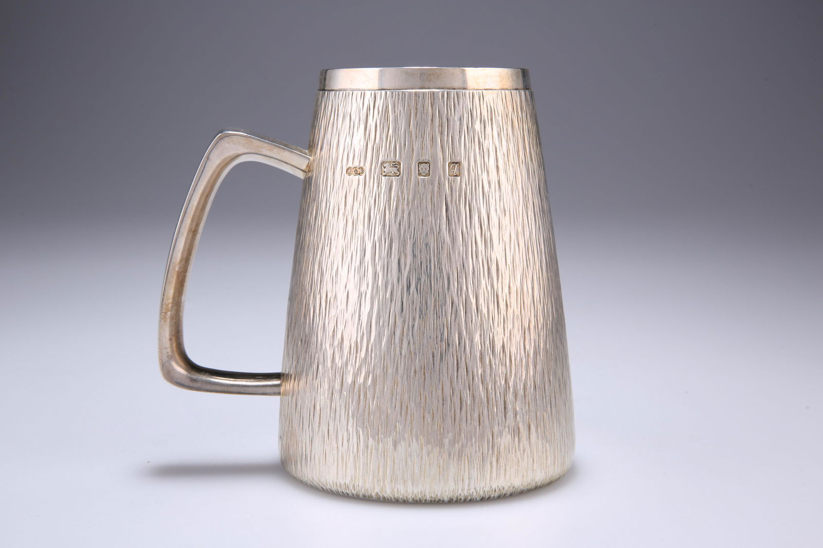 AN ELIZABETH II SILVER MUG, by Gerald Benney, London: AN ELIZABETH II SILVER MUG, by Gerald Benney, London 1971, large, of tapering cylindrical form, the chased bark-effect outer edge with plain rim and handle, gilded to interior. 13cm high, 15.4 troy o