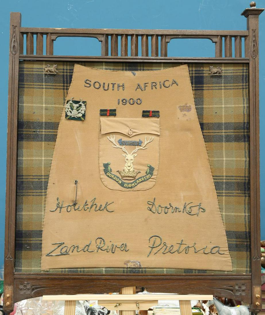 A WOODEN FIRESCREEN PANEL, THE FEET REMOVED, DECORATED: A WOODEN FIRESCREEN PANEL, THE FEET REMOVED, DECORATED TO COMMEMORATE THE GORDON HIGHLANDERS IN SOUTH AFRICA 1900, the central motif being in the form of a khaki kilt with bullion embroidered panels