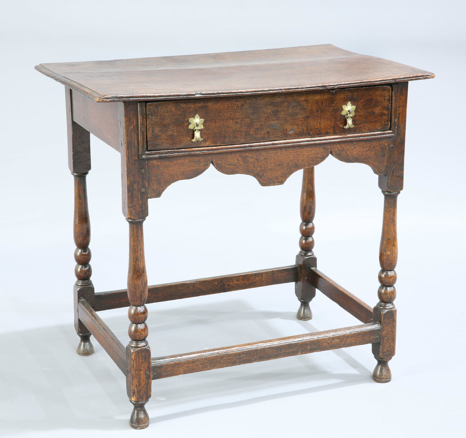 A QUEEN ANNE OAK SIDE TABLE, the moulded rectangular: A QUEEN ANNE OAK SIDE TABLE, the moulded rectangular top above a frieze drawer with brass drop handles over a shaped apron, raised on baluster and bobbin turned legs, continuing to blocks joined by s