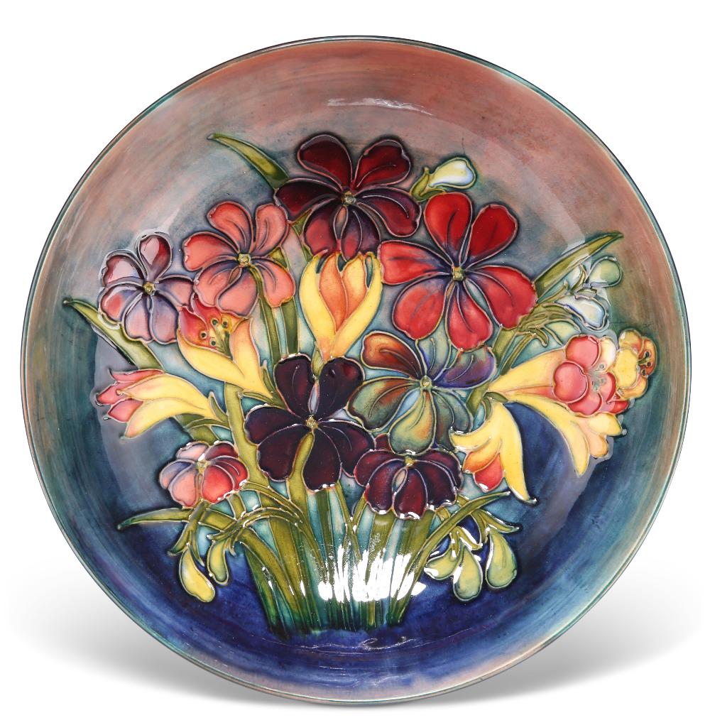 A WALTER MOORCROFT FLAMBÃ‰ POTTERY BOWL, shallow form, 'Spring Flowers' pattern, tubelined and: A WALTER MOORCROFT FLAMBÃ‰ POTTERY BOWL, shallow form, 'Spring Flowers' pattern, tubelined and painted in tones of red, yellow and green, to a graduated red-blue well and a blue exterior, blue wash