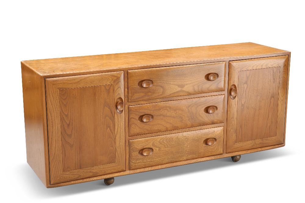 AN ERCOL LIGHT ELM SIDEBOARD, with a pair of cupboard doors flanking three drawers, moving on castor: AN ERCOL LIGHT ELM SIDEBOARD, with a pair of cupboard doors flanking three drawers, moving on castors. 68cm high, 155.5cm wide, 44cm deep
