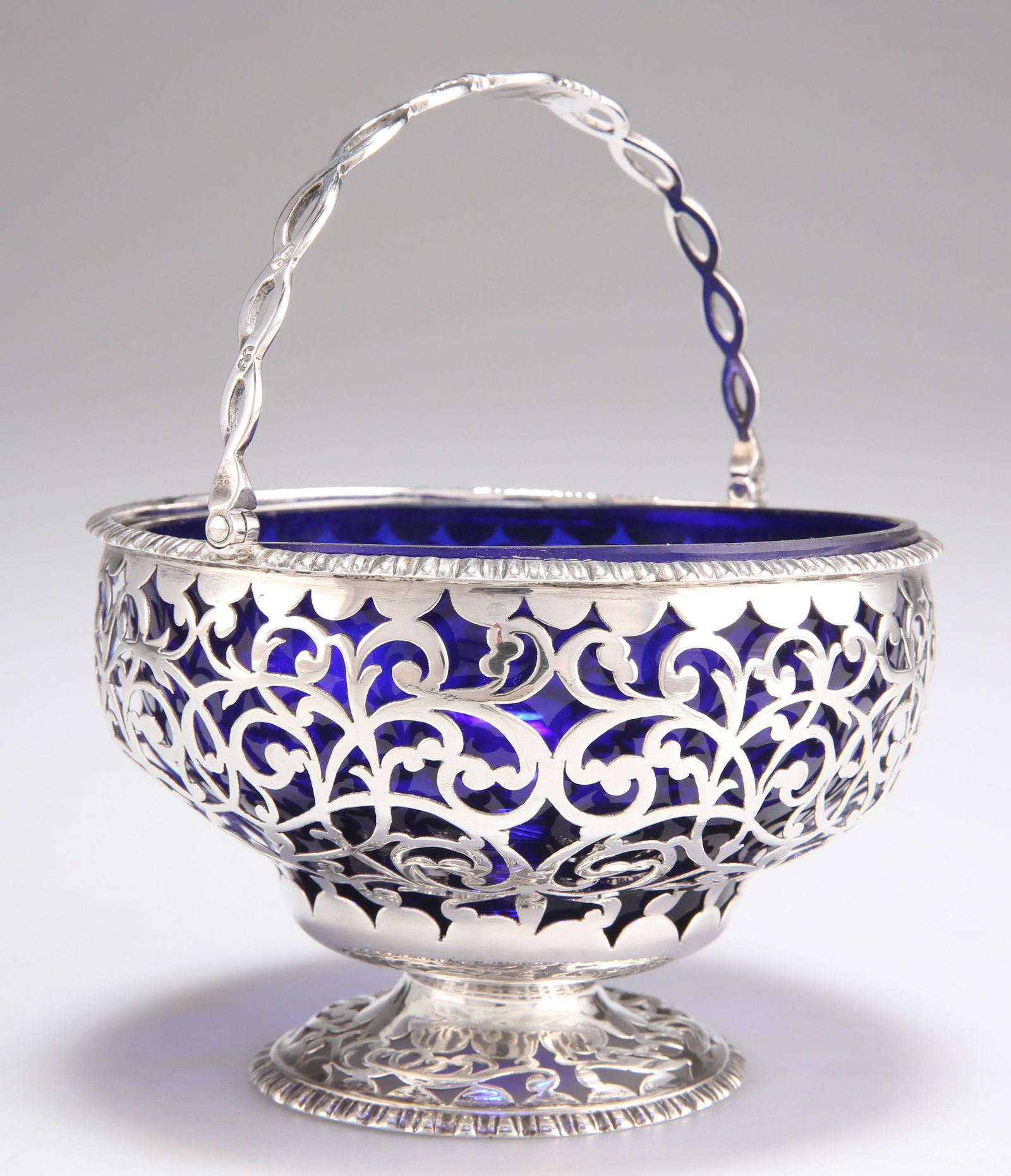 A VICTORIAN SILVER SUGAR BASKET: A VICTORIAN SILVER SUGAR BASKET marks rubbed, probably by Thomas Smily, London 1851, circular with openwork swing-handle, the sides pierced with scrollwork, blue glass liner. 7.5cm high excl. handle,