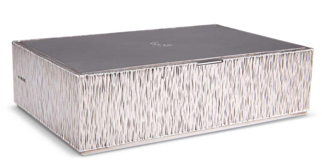 AN ELIZABETH II SILVER CIGARETTE BOX: AN ELIZABETH II SILVER CIGARETTE BOX by Gerald Benney, London 1965, rectangular, the hinged polished cover engraved with a crest, the four sides with a bark effect ground. 4.3cm high, 15cm wide, 10cm