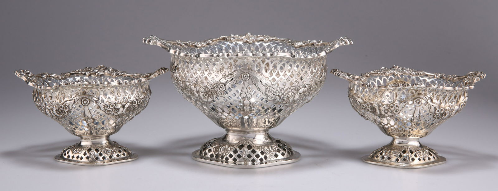A SET OF THREE VICTORIAN SILVER TABLE DISHES: A SET OF THREE VICTORIAN SILVER TABLE DISHES by Charles Stuart Harris, London 1899 and 1900, each of shaped oval form with a domed foot, the sides pierced and embossed with floral swags. (3) Largest 1