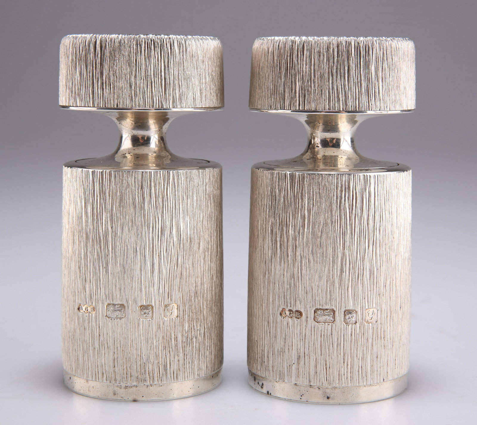 A PAIR OF ELIZABETH II SILVER SALT AND PEPPER MILLS: A PAIR OF ELIZABETH II SILVER SALT AND PEPPER MILLS by Gerald Benney, London 1998, stamped BENNEY to the underside, each with bark effect textured ground. (2) 11cm high, 21.7 troy ounces gross