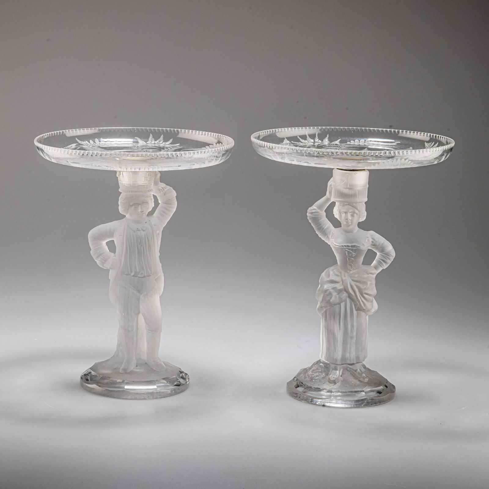 A PAIR OF FIGURAL TAZZAS, BY JOHN FORD & CO, HOLYROOD GLASSWORKS, EDINBURGH, CIRCA 1870: A PAIR OF FIGURAL TAZZAS, BY JOHN FORD & CO, HOLYROOD GLASSWORKS, EDINBURGH, CIRCA 1870 modelled as a gentleman and his female companion in frosted glass, each standing with one hand upon their hip, h