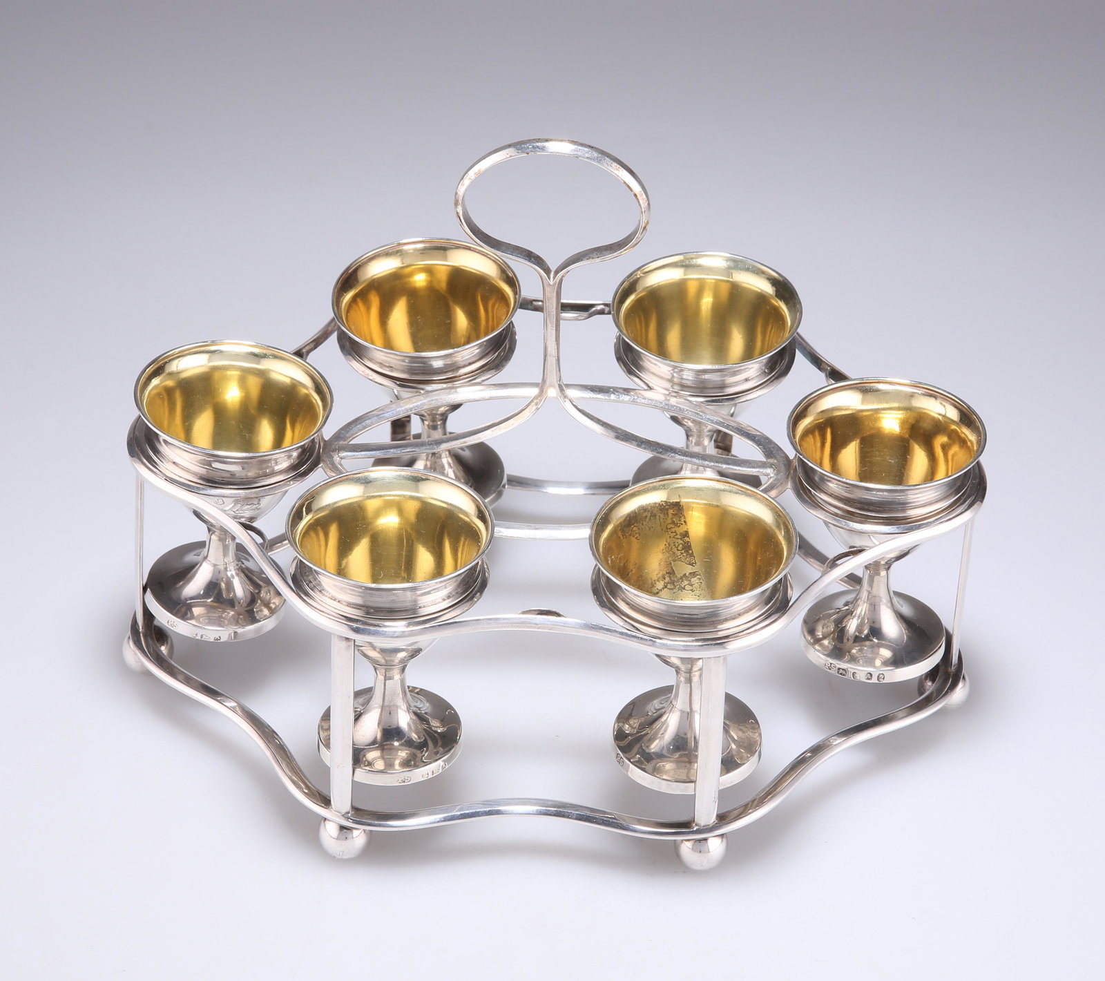 A GEORGE III SILVER EGG CRUET: A GEORGE III SILVER EGG CRUET by Paul Storr, London 1796, shaped-oval frame with wavy outline, fitted with six removable egg cups, with gilt interiors, centred with a carrying handle, the whole on six