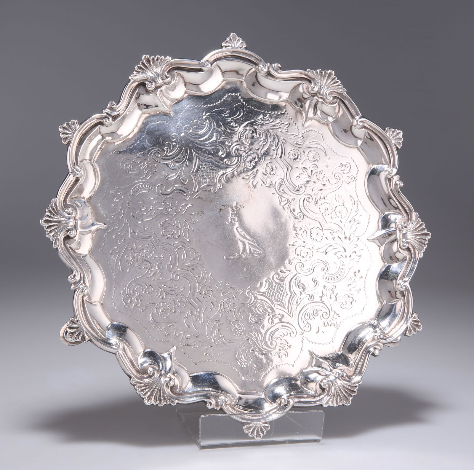 A GEORGE III SILVER SALVER: A GEORGE III SILVER SALVER by Robert Garrard I, London 1806, with flat-chased decoration to the base, engraved with a crest, the shaped rim cast with scrolls and scallop shells, raised on three hoof f