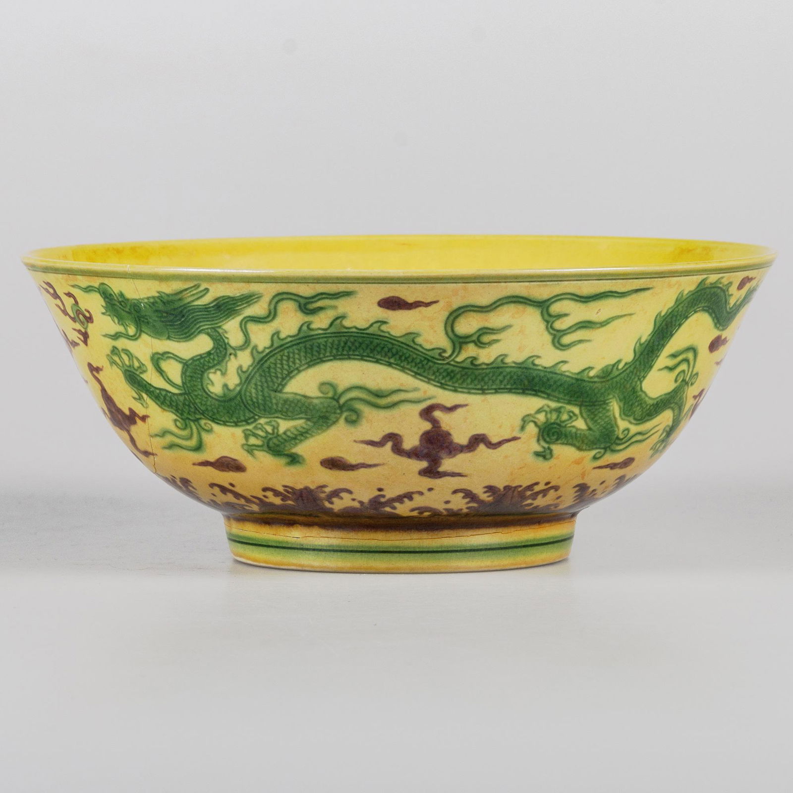 A CHINESE YELLOW GROUND GREEN AND AUBERGINE ENAMELLED 'DRAGON' BOWL: A CHINESE YELLOW GROUND GREEN AND AUBERGINE ENAMELLED 'DRAGON' BOWL the five-clawed dragons chasing flaming pearls above a band of waves, the interior with incised clouds, the base bears six-character