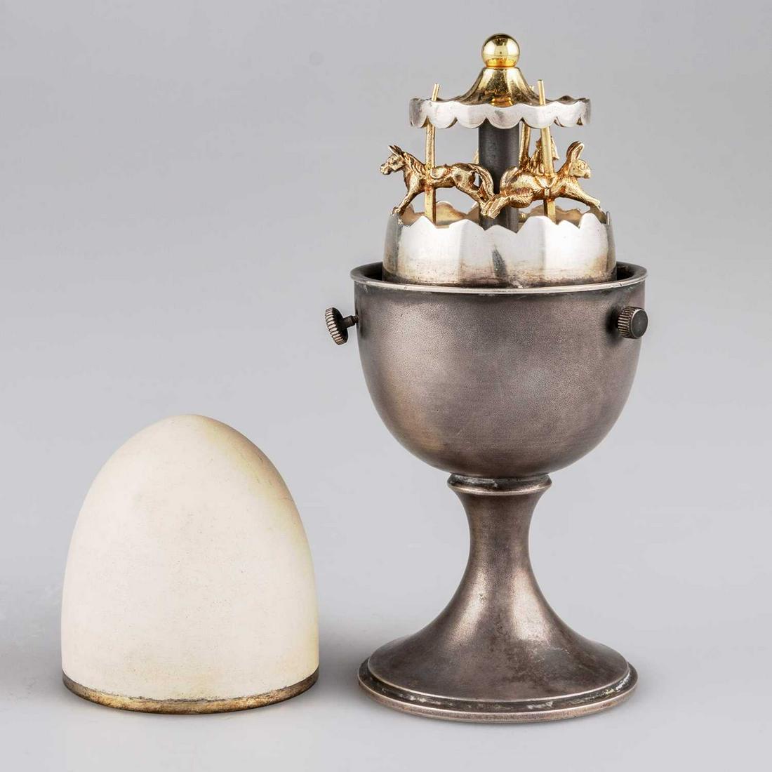 AN ELIZABETH II SILVER NOVELTY EGG TIMER: AN ELIZABETH II SILVER NOVELTY EGG TIMER by Anthony Gordon Elson, London 1980, realistically modelled as a silver egg cup and egg, the removable porcelain-covered egg top reveals a carousel with rab