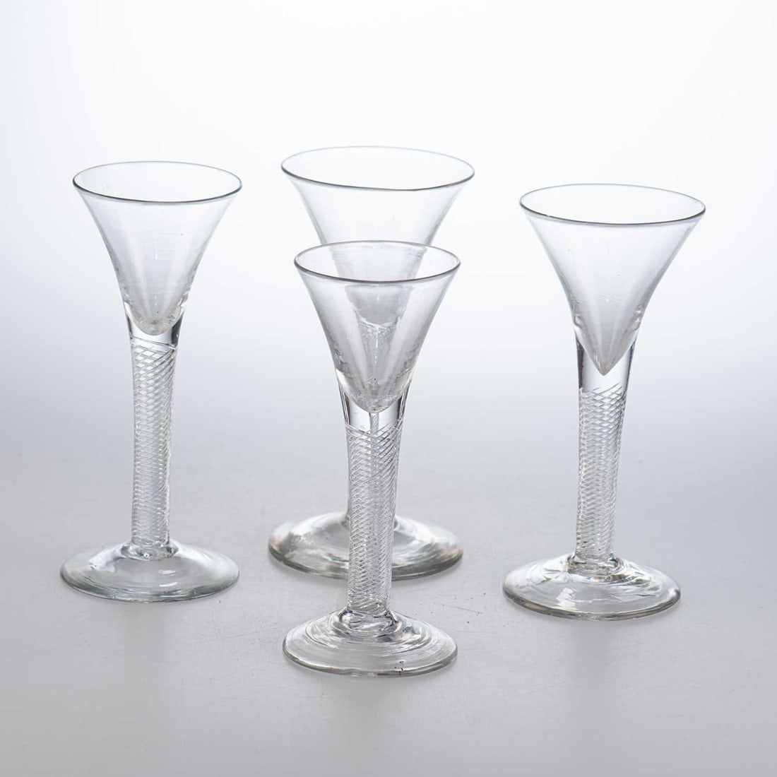 FOUR 18TH CENTURY WINE GLASSES: FOUR 18TH CENTURY WINE GLASSES each with a funnel bowl and air-twist stem raised on a circular foot. (4) Tallest 16.8cm