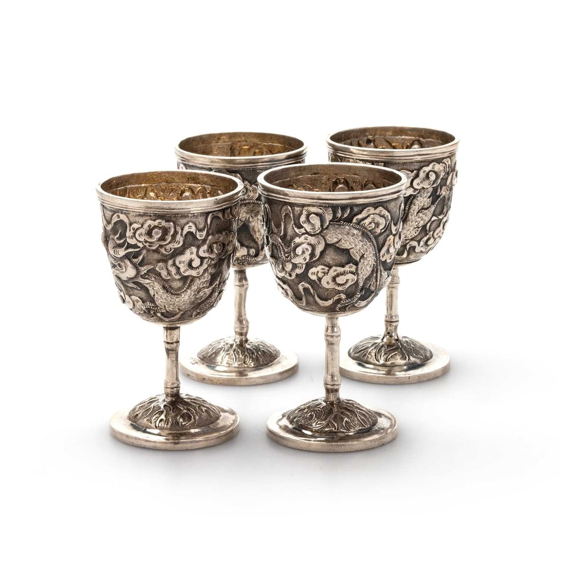 A SET OF FOUR CHINESE SILVER EGG CUPS: A SET OF FOUR CHINESE SILVER EGG CUPS embossed with dragons amongst clouds, on bamboo stems and circular spreading feet. (4) 7.5cm high, 5 troy ounces gross wear commensurate with age, some minor den